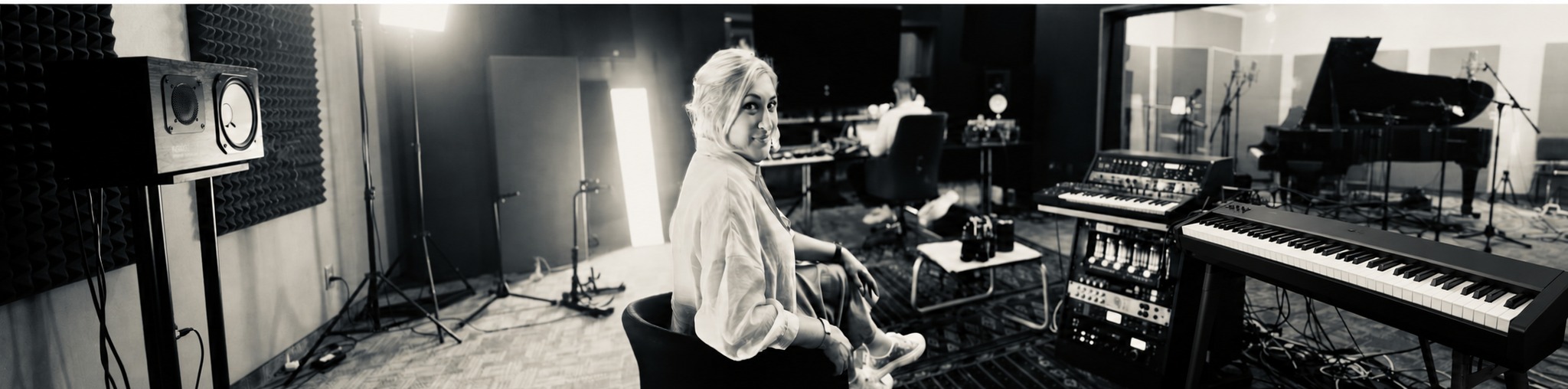 Larissa Tormey seated in a recording studio with keyboards, a piano and production equipment